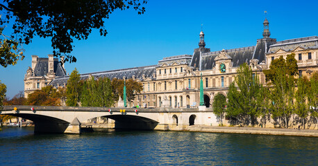 View of Pont du Carrousel across Seine river leading to arched entrance to Louvre palace courtyard,...