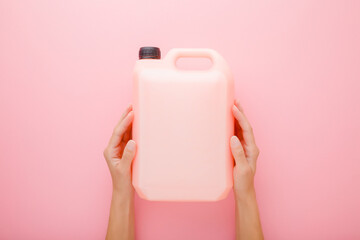 Young woman hands holding 5 L plastic container on pink table background. Pastel color. Cleaning...
