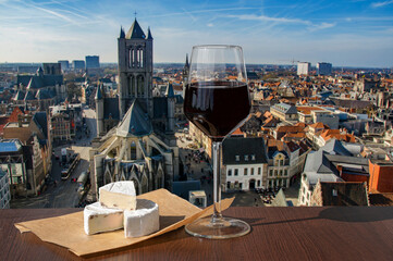 Glass of red wine with brie cheese against view of big cathedral in Ghent, Belgium