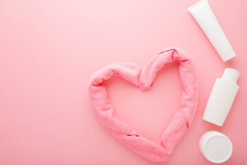 White toiletries and heart shape created from towel on light pink table background. Pastel color....