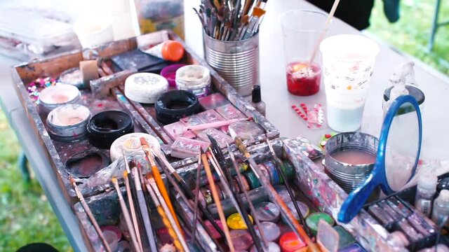 Table with paints and brushes for theatrical makeup during an off-site event. Many colors for painting on the face and powdered makeup applied to the body, these products can cause allergic reactions.