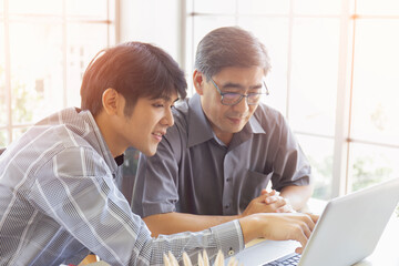 Obraz premium An elderly Asian man is learning how to trade online through the Internet with a young man who teaches him.