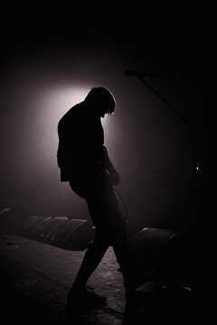 Monochrome photography. A slightly blurred silhouette of a young man with a guitar in the smoke, illuminated by a contour light.