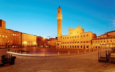 Early morning view of beautiful Campo Square (Piazza del Campo) in the center of Siena, a medieval town in Tuscany Italy, with Palazzo Pubblico & the famous Mangia Tower (Torre del Mangia) in twilight