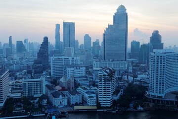 Morning scenery of Bangkok City in bird's eye view ~ Urban skyline of Bangkok in misty twilight, with hotels & office towers by Chao Phraya River & MahaNakhon amid modern skyscrapers under dawning sky