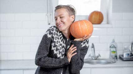 Beautiful woman in sweater with orange pumpkins in white kitchen