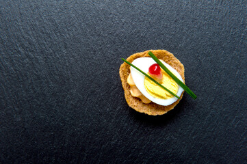 Tasty canapes with egg on black background