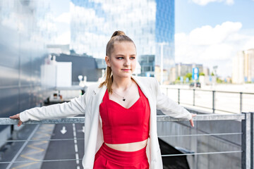 Obraz premium young blonde schoolgirl in a red suit and a white jacket posing in the parking lot