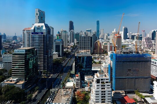 Cityscape of Bangkok, the fast developing capital city of Thailand, with busy traffic on the street and the famous landmark MahaNakhon Tower amid high rise buildings in background under blue sunny sky