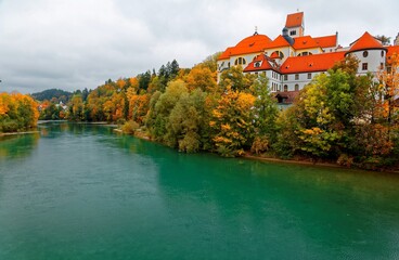 Fototapeta na wymiar Fall scenery of beautiful Lech River with the majestic landmark architecture, Hohes Schloss Castle, in the background and colorful autumn trees by the riverside, in Fussen, Bavaria, Germany, Europe