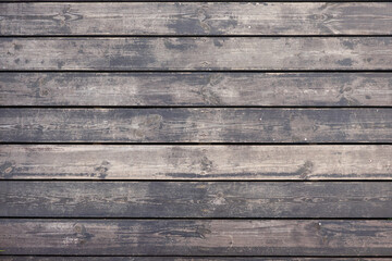 A fragment of a wooden flooring of a street footpath made of planks. The dark paint has worn off, the wood structure is visible. Background. Texture.