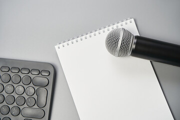 Podcast concept. White notebook with blank sheet. Black microphone, notebook and keyboard. Audiobook and podcasting. Audio technology. Home school teaching.