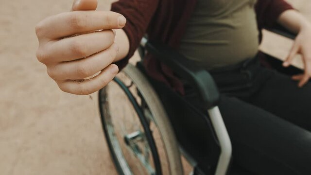 close up, hand of disabled person in the wheelchair playing with the sand on the beach. High quality 4k footage