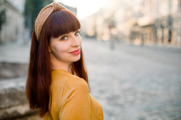 Outdoor city close up portrait of beautiful red haired young woman wearing yellow dress and knitted...