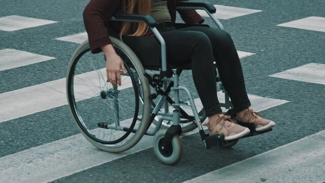 Young unrecognizable handicapped woman in wheelchair crossing street carefully. High quality 4k footage