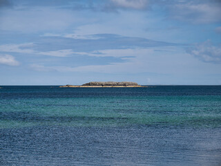 On a sunny day with calm, turquoise waters and a blue sky, the rocky outcrop of Black Skerry in the mouth of Otters Wick off the island of Yell in Shetland, Scotland, UK