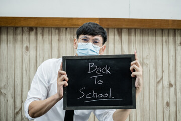 Back to school. Asian male students wearing masks, holding blackboard labeled Back to School. College male Back to School after Pandemic Coronavirus Disease 2019