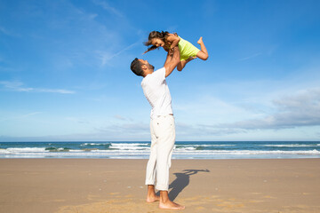 Cheerful excited dad holding girl and throwing hands up in air. Handsome father and little daughter having fun outdoors, playing active games. Family outdoor activities concept