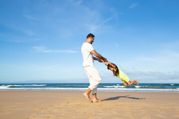 Young handsome dad having fun with little daughter on beach, playing active games, holding girls...