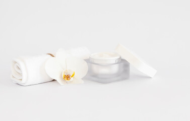 White towel with white orсhid flower and face cream on white copy space background. Facial treatments concept.