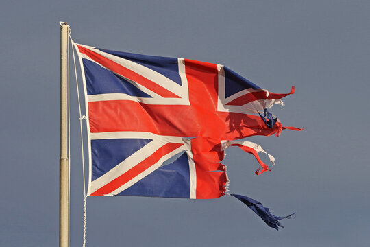 British flag or Union Jack torn and tattered flying in the winter by the sea in Italy representing the disaster of Brexit	