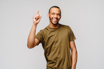 Fototapeta premium Joyful friendly african-american young man in green t-shirt pointing up by finger at copy space