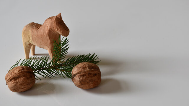 Kleines Holzpferd, N&uuml;sse, Fichtenreisig vor wei&szlig;em Hintergrund als weihnachtliches Motiv f&uuml;r Advent und festliche Saison als Gru&szlig;karte und Tischkarte