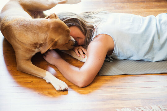 A woman and her dog lie on the floor together cuddling.