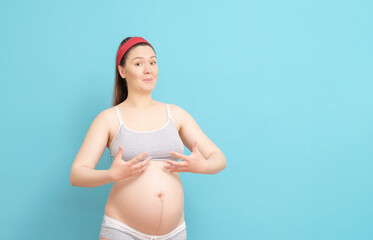 young pregnant woman is surprised that her breasts have grown on blue background