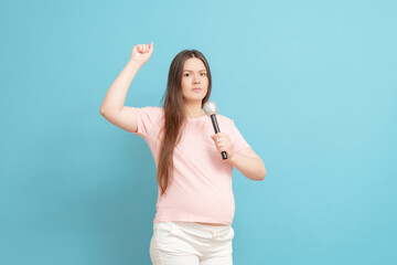 aggressive young pregnant woman shouts into the microphone in pink t-shirt on blue background, protest,