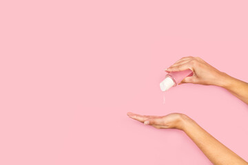 Manosde mujer desinfectandose con gel antibacteriano sobre un fondo rosa pastel liso y aislado. Vista de frente. Copy space