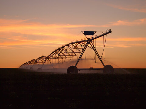 Pivot water system on a farm field at sunset, agriculture irrigation machine silhouette - Powered by Adobe