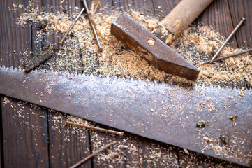 Old vintage hammer, wood saw, nails and sawdust on a wooden background, close-up, selective focus.