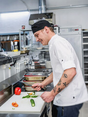 Young cook in white uniform working at the kitchen of the restaurant