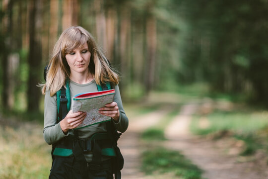 Young woman with backpack looking at map hiking in summer forest