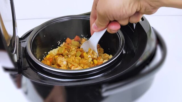 Macro Video of a multicooker. The man opens the pan and mixes the dish. Steam can be seen from the cooked food. The concept of cooking automation and ease in the kitchen.