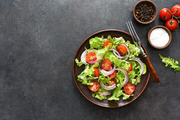 Vegetable salad with tomatoes, red onions and sauce on a black background.