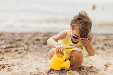 Little girl using yellow watering can on beach