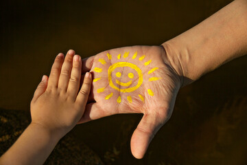 children's palm on man's hand with yellow smiling sun stretches out his hand to child's palm