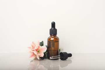 A glass dropper bottle with a pippette with black rubber tip and beautiful flower on grey background. Nature Skin concept. Organic Spa Cosmetics. Close up.