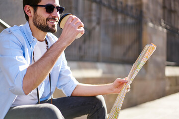 Delighted man drinking coffee while reading map