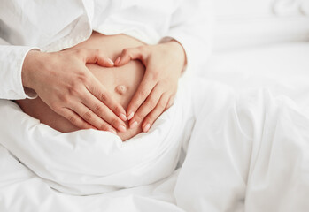 Fototapeta na wymiar Crop pregnant female gesturing heart on tummy in bed