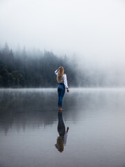 Fototapeta na wymiar Young person standing in the foggy lake near the wilderness forest. Lifestyle,hipster style.