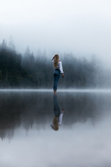 Fototapeta na wymiar Young woman standing in misty autumn lake in the wilderness forest.