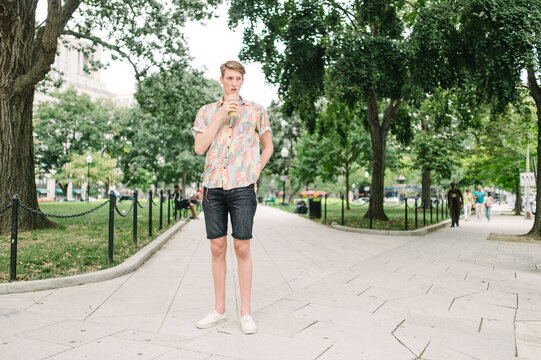 Insanely tall preppy hipster drinking an iced coffee while standing at a corner at the park