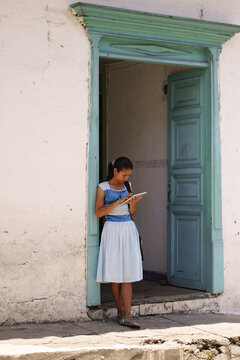 Young latin woman in dress at turqoise colonial door using tablet