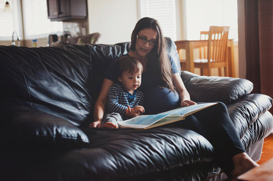 Young mom and 2 year old son reading together on couch