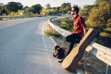 Man with his guitar leaning on the guardrail of the road