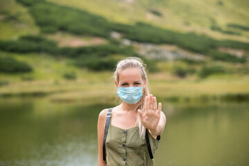 Young woman travels in the mountains. A tourist travels in a medical mask. A medical mask on the girl's face. Coronavirus pandemic tourism day
