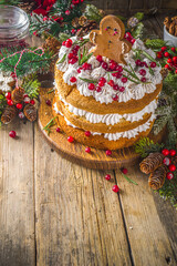 Festive Christmas gingerbread cake with whipped cream cheese, decorated cranberry and gingerbread cookies, wooden background with christmas decor copy space